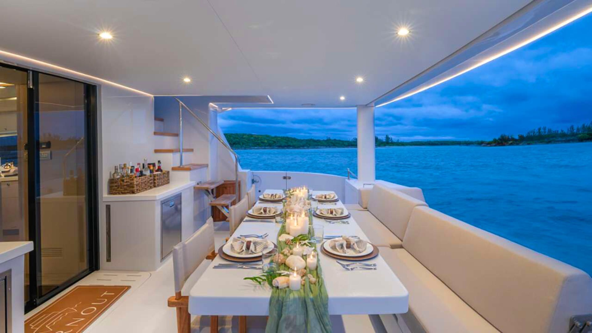 Candlelit aft-deck dinner table set at dusk aboard a crewed catamaran