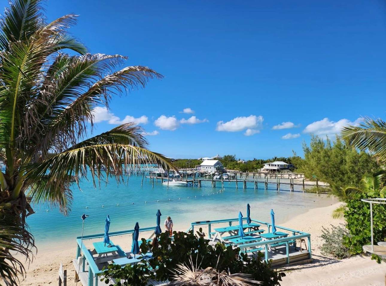 Turquoise picnic tables on a beach-bar deck beside a dock on the Sea of Abaco