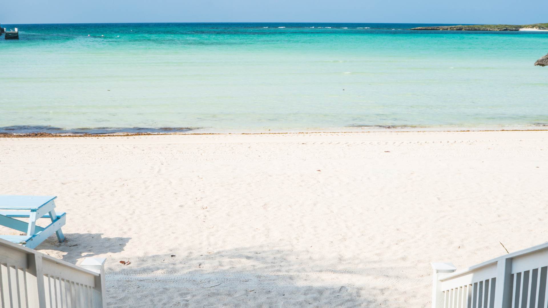 A picnic table on white sand above turquoise shallows.