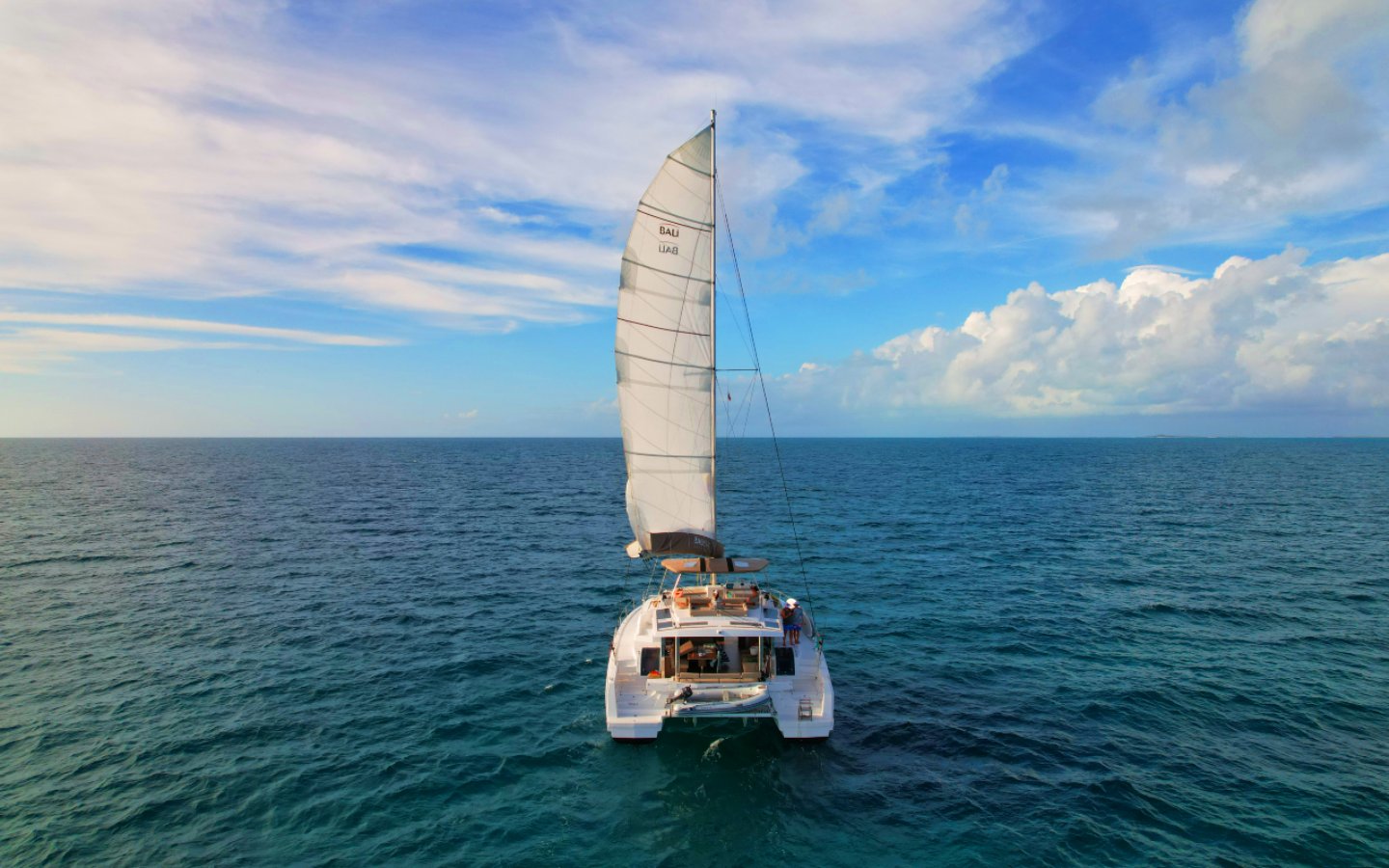 Crewed sailing catamaran running downwind under full sail in Bahamas water
