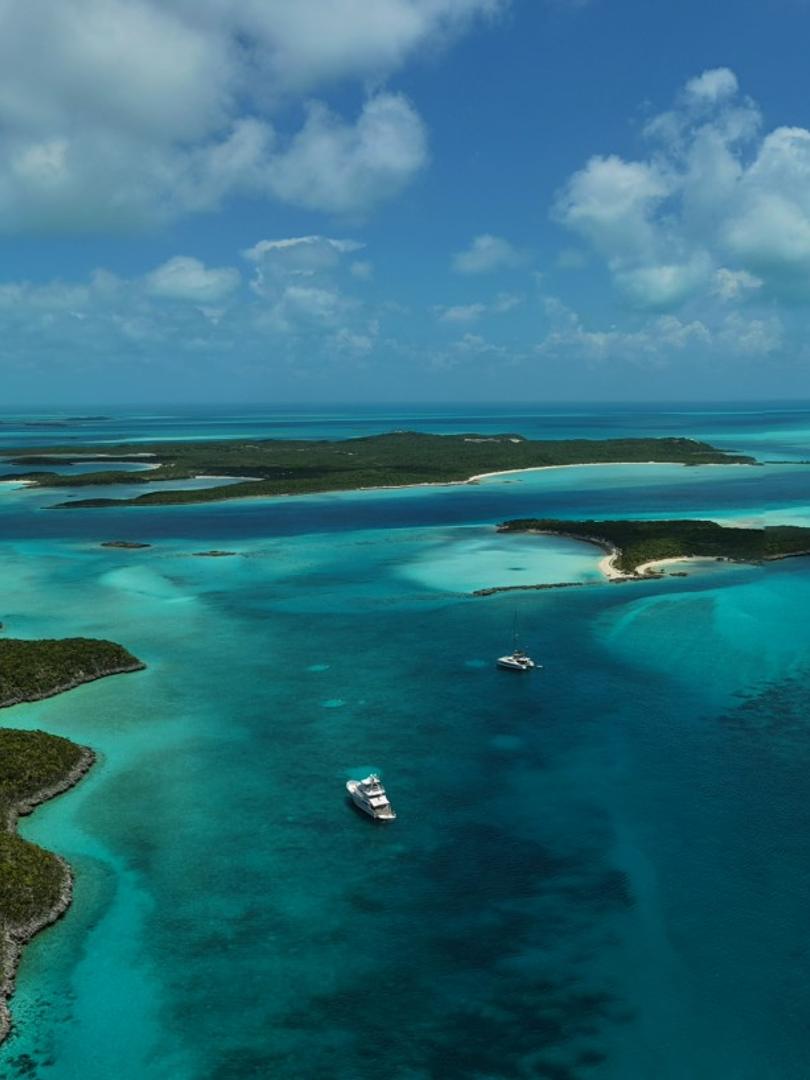 Vertical aerial of yachts at anchor in banded turquoise between low green Bahamas cays