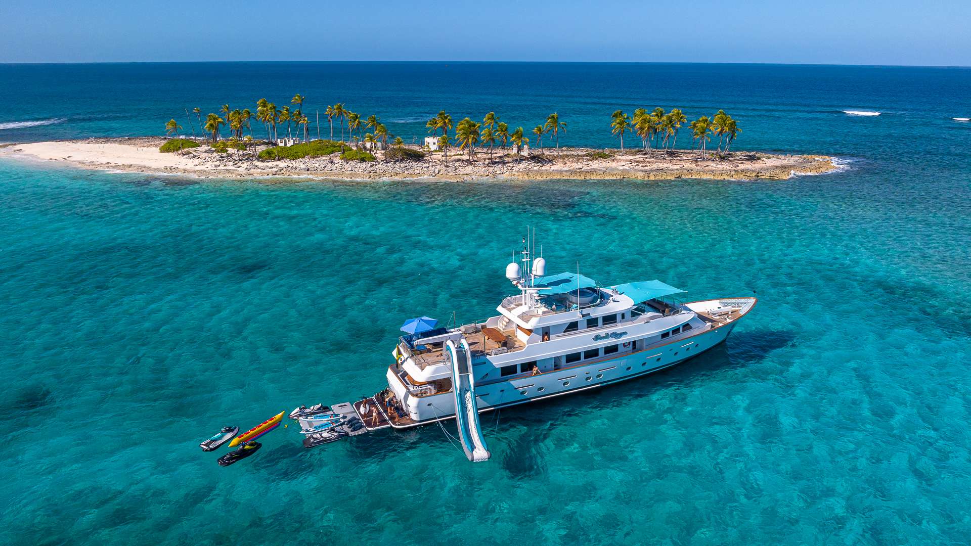 Motor yacht with a waterslide rigged, anchored off a palm-covered Bahamas cay