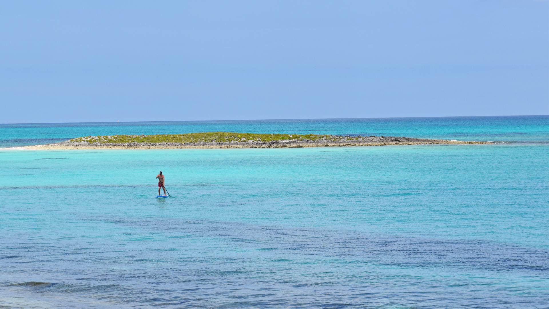 A paddleboarder crossing glassy flats off a low scrub cay