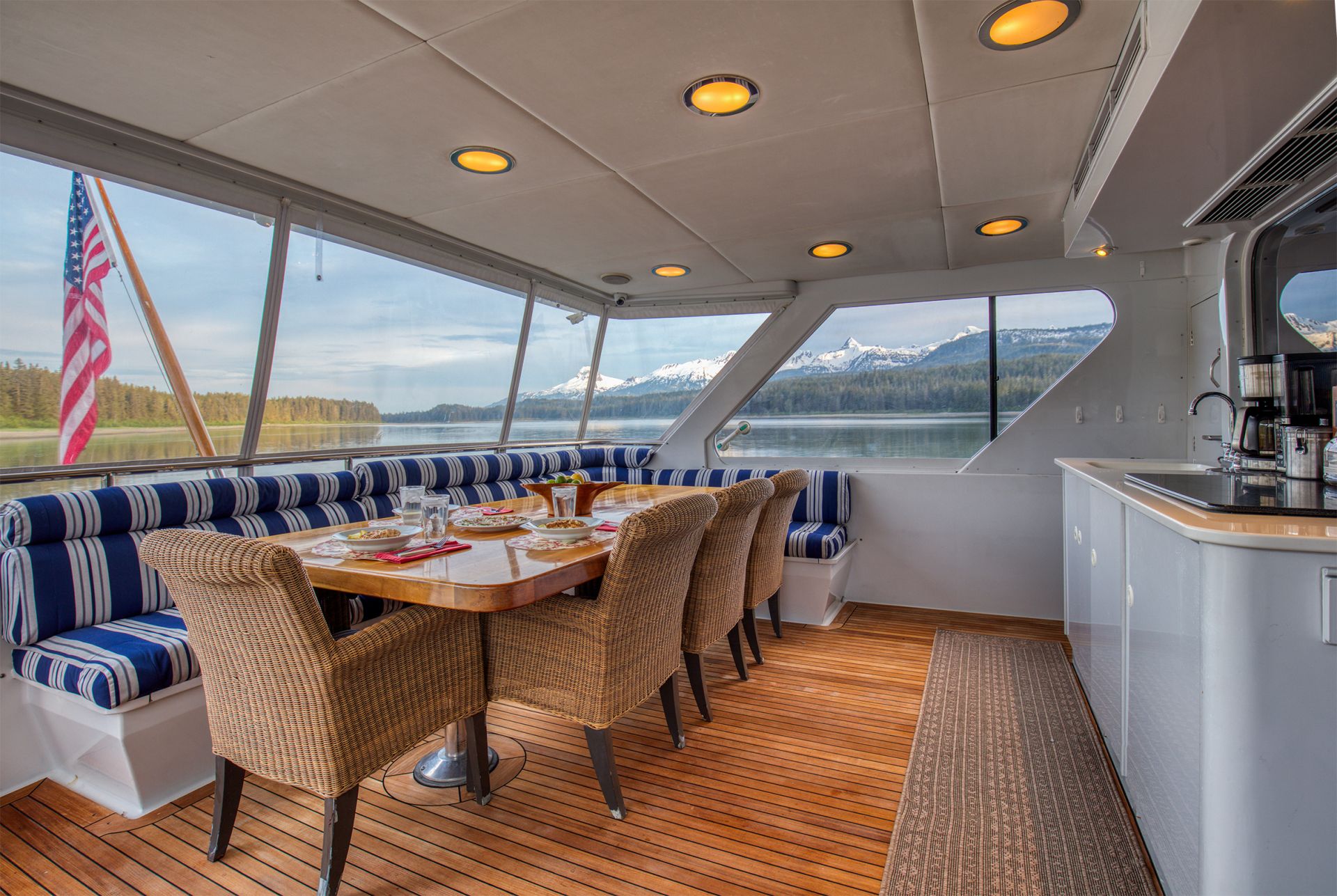 Aft-deck dining table set aboard a motor yacht, snow-capped peaks across the channel