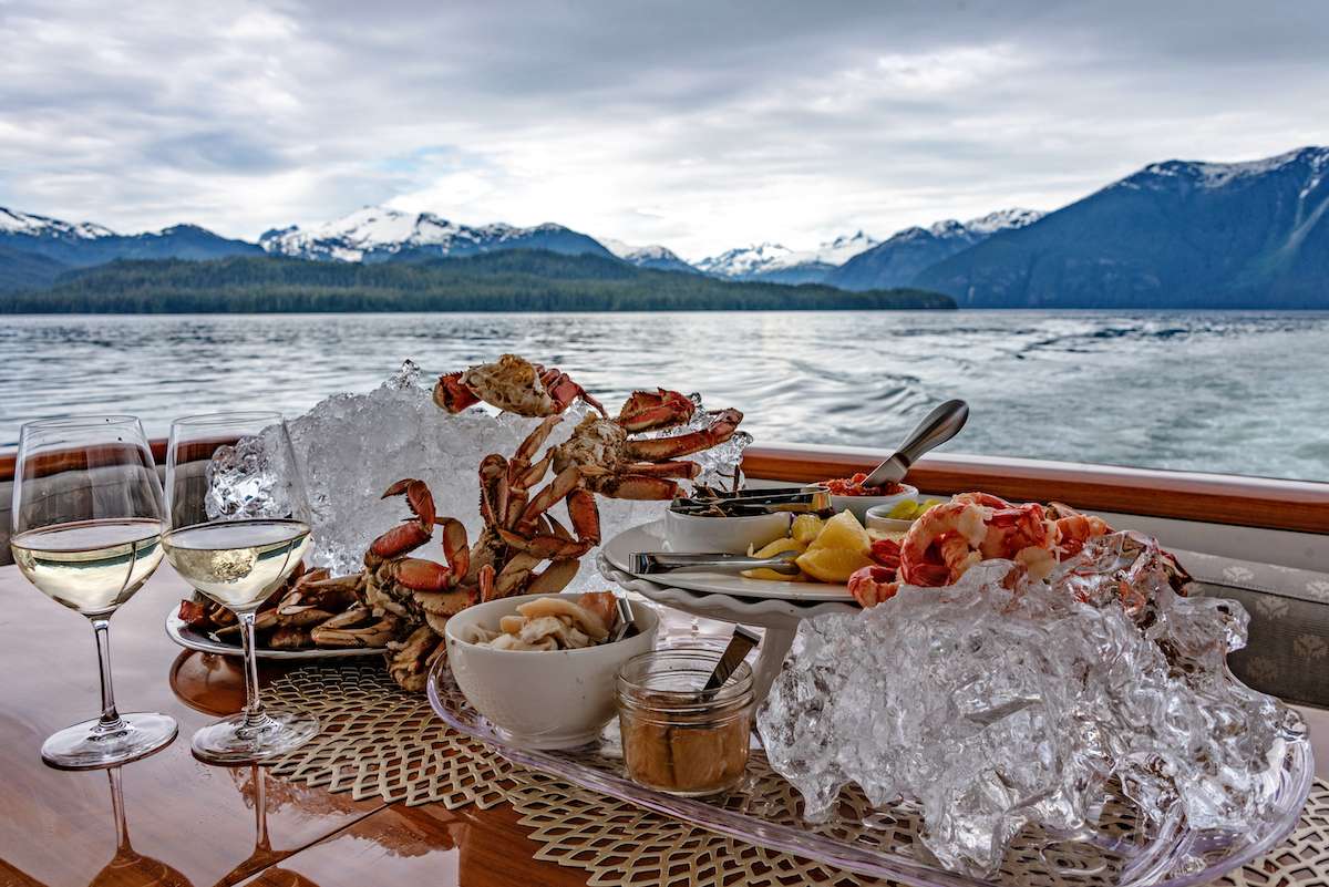 Dungeness crab and spot prawns served over glacier ice on deck, snow peaks across the channel