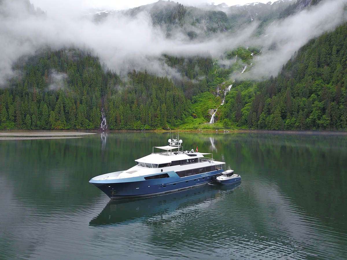 Motor yacht at anchor in a fog-draped fjord, waterfalls cascading down the forested wall