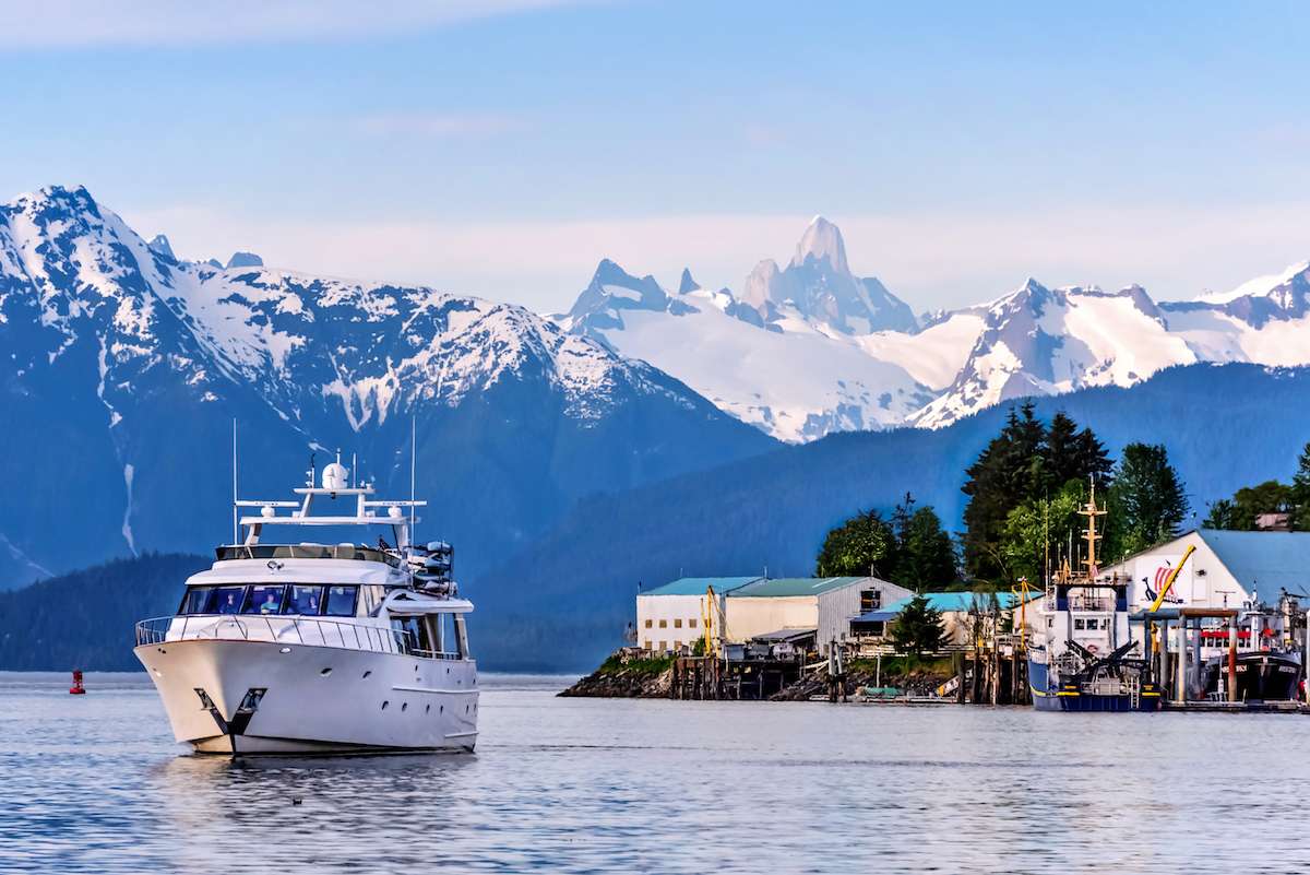 A classic motor yacht arriving at the Petersburg waterfront, Devil's Thumb's spire on the horizon behind — the working fishing town at the north end of Mitkof Island where this route embarks.