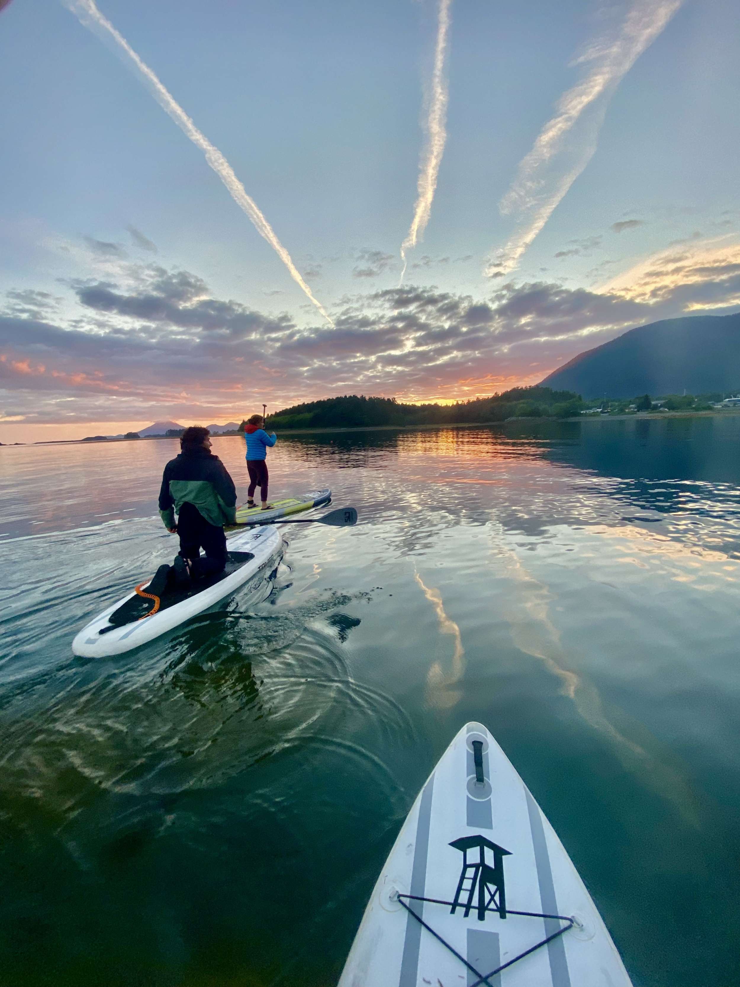 Two paddleboarders on calm water at sunset, a distant volcanic peak on the horizon.