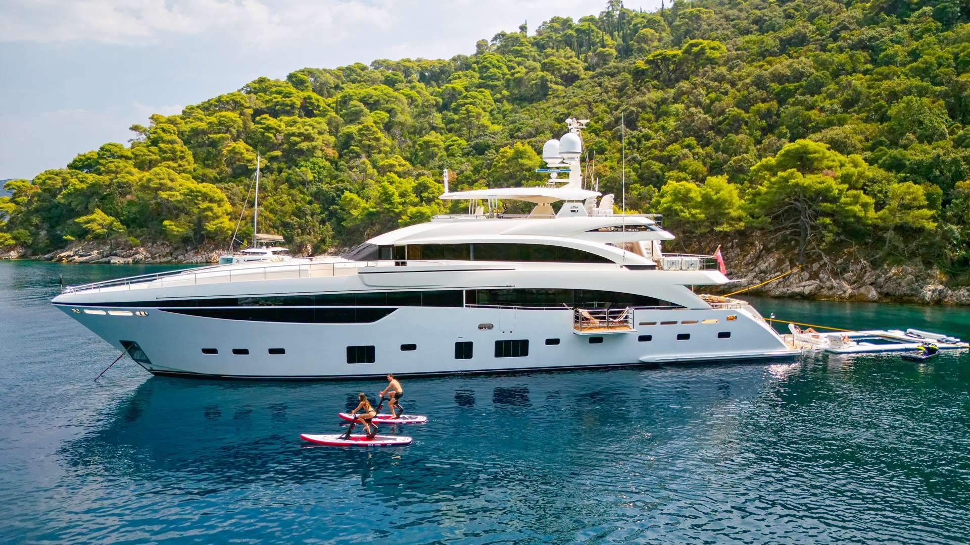Crewed motor yacht at anchor with paddleboards deployed in a Mediterranean cove