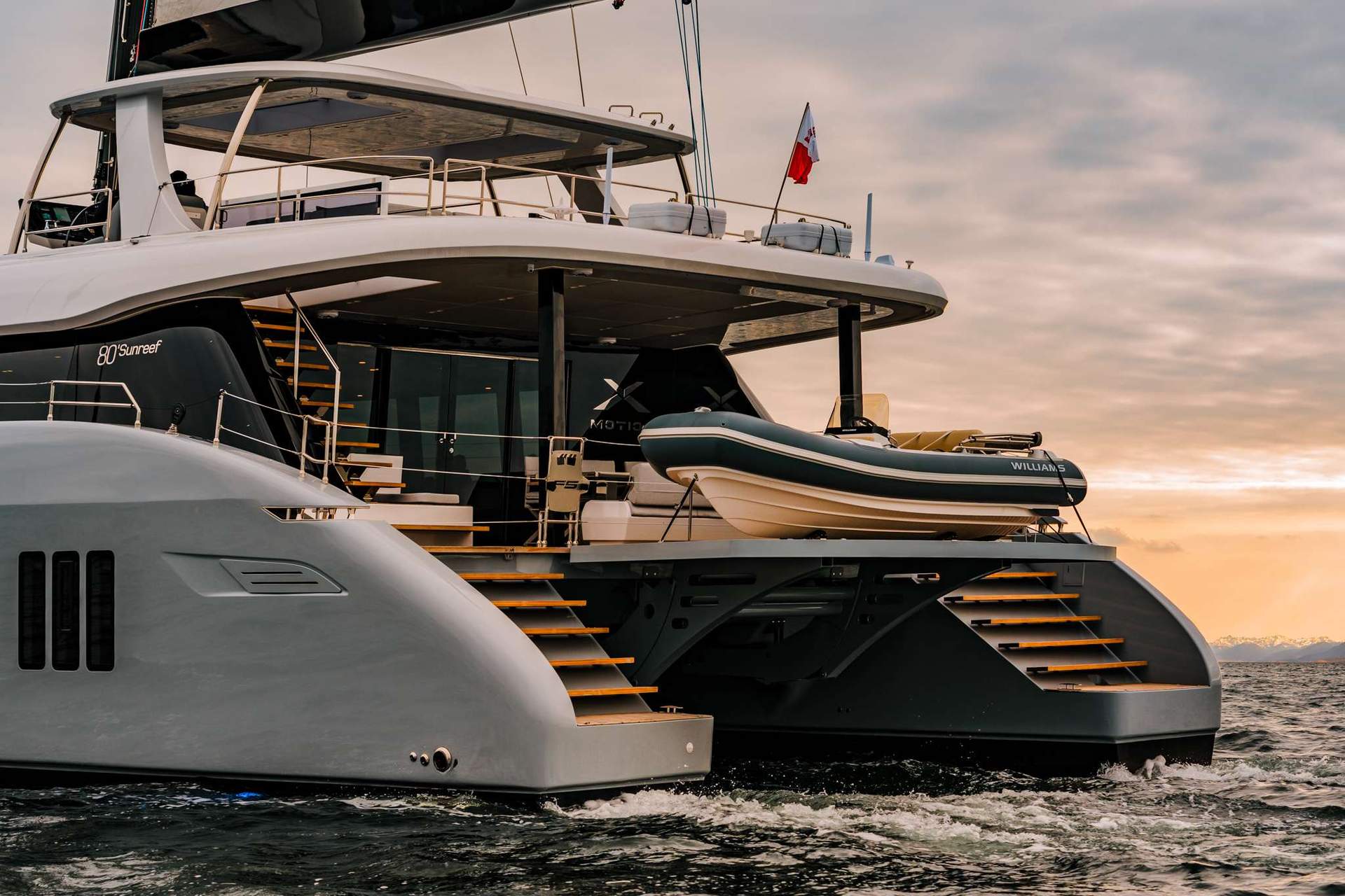 Crewed catamaran stern with tender at sunset