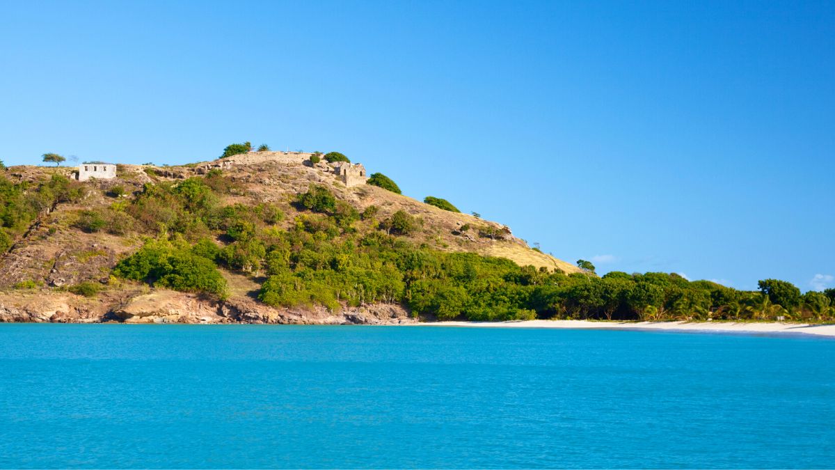 Deep Bay — a white-sand crescent with the 1905 wreck of the Andes snorkelable mid-anchorage and Fort Barrington on the headland above. Staging north for the Barbuda crossing.