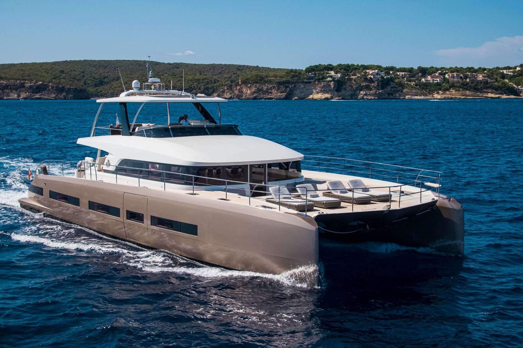 Crewed catamaran underway off Mallorca's southwest coast with the Tramuntana foothills behind