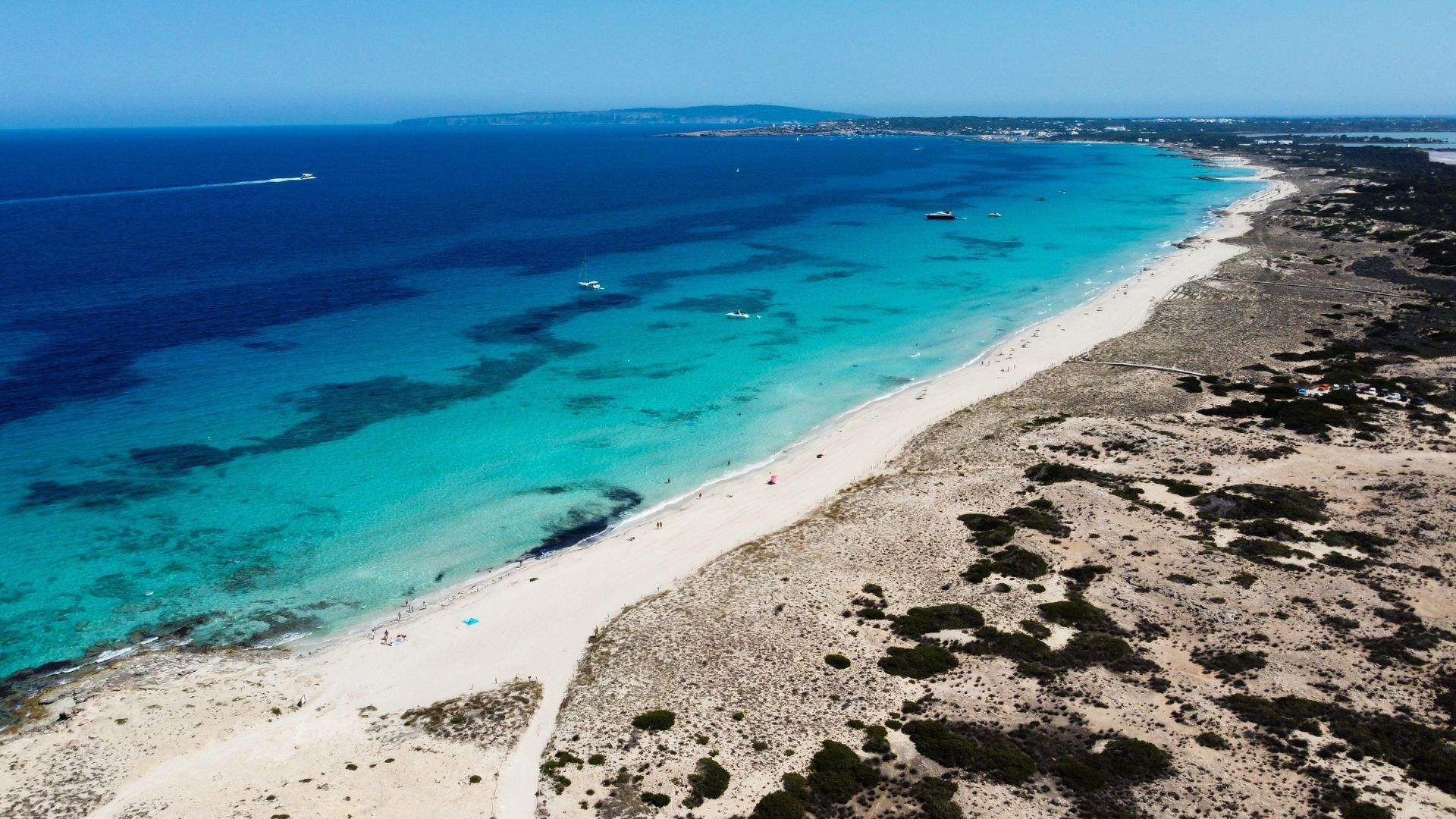 Es Trenc beach aerial — long white-sand south Mallorca beach with yacht at anchor offshore.