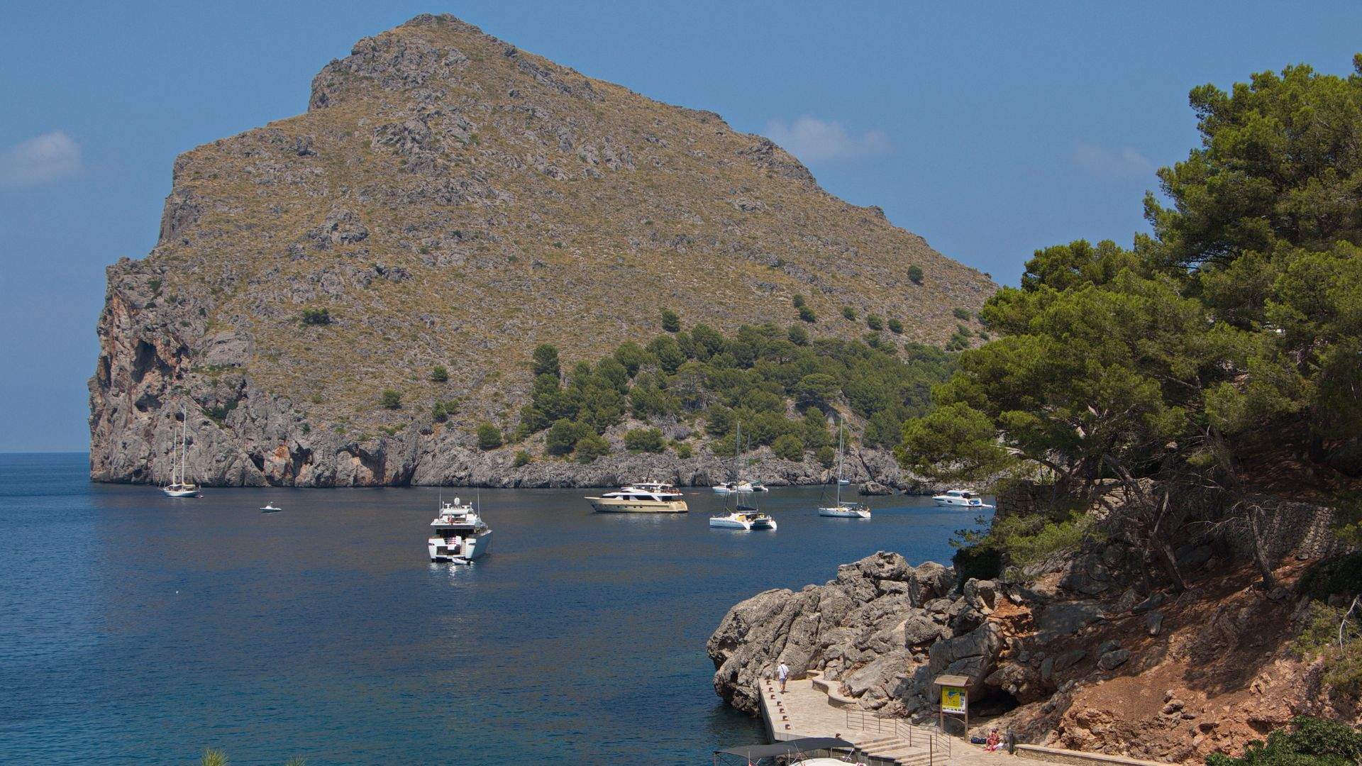 A stone-and-sand cove at the base of Mallorca's tallest mountain. The cliff walls rise straight from the water on both sides of the cove.