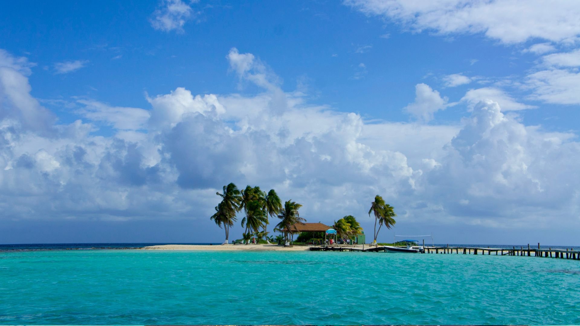 Goff's Caye—a two-acre palm-covered reef island with a long wooden dock and clear turquoise water.