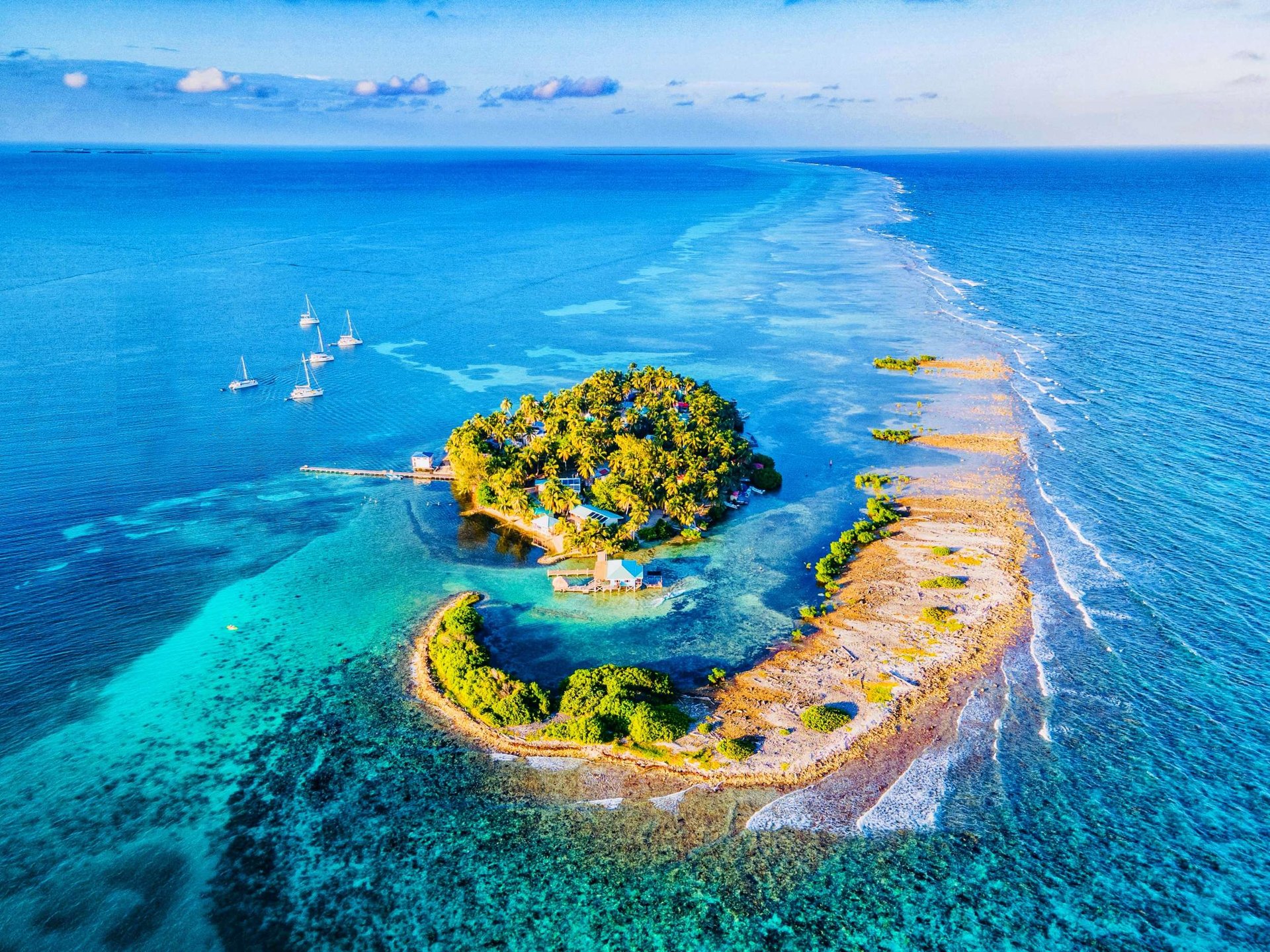 Aerial of a Belize mangrove caye with sailing yachts anchored off the side.
