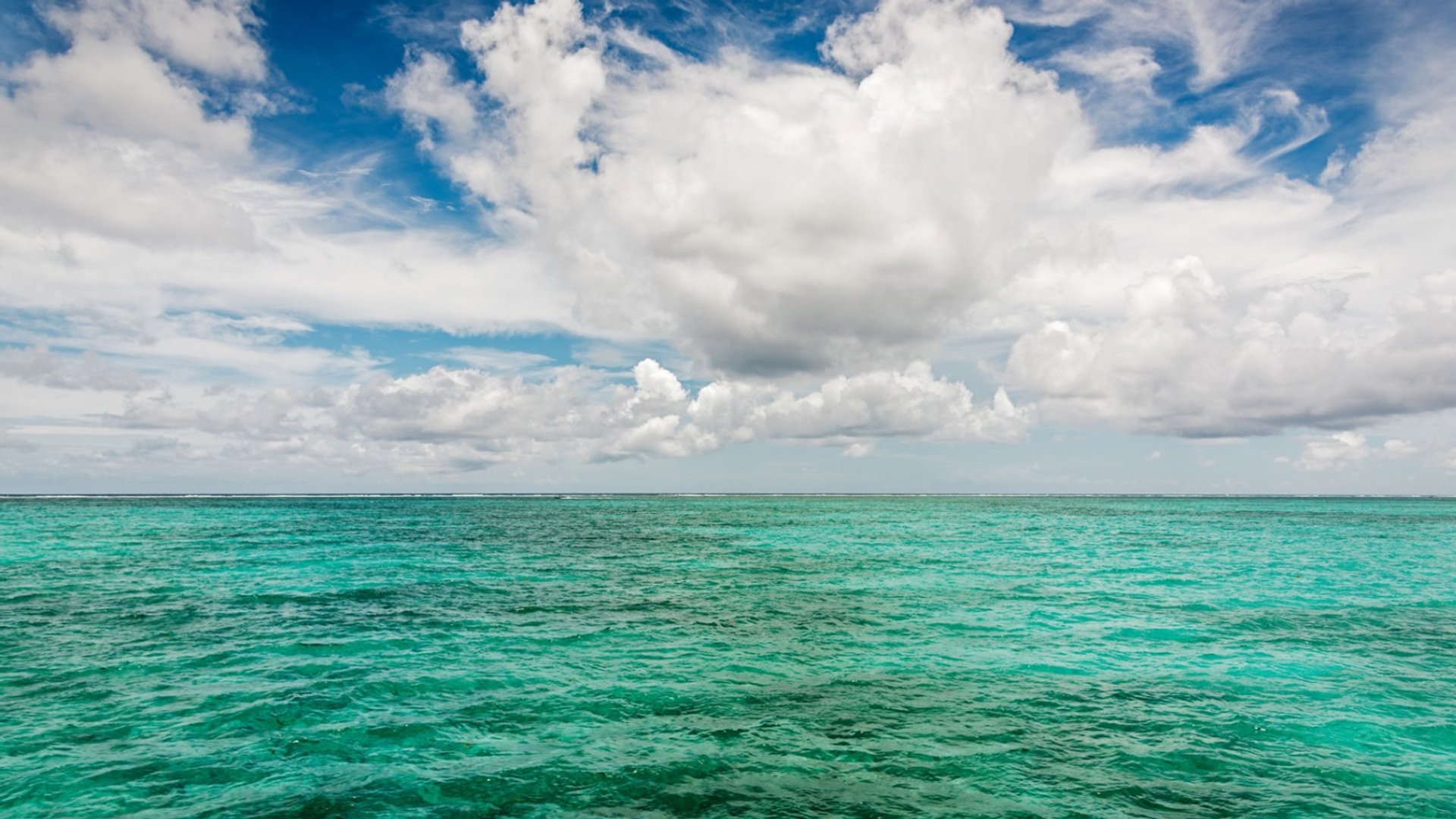 Turquoise barrier reef seascape with scattered clouds on the horizon.