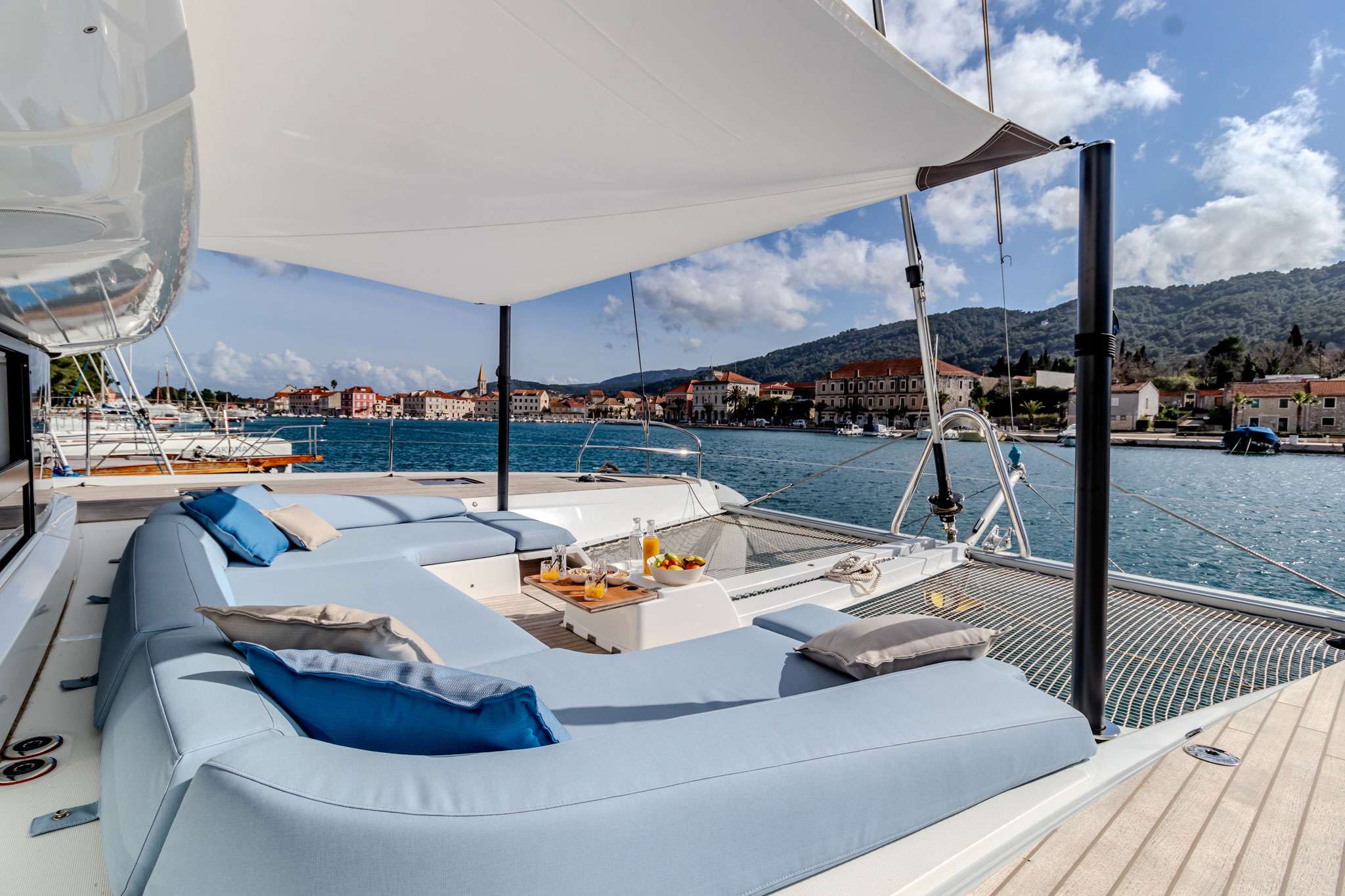 Sundeck lounge aboard a crewed catamaran with a Dalmatian coastal town across the water