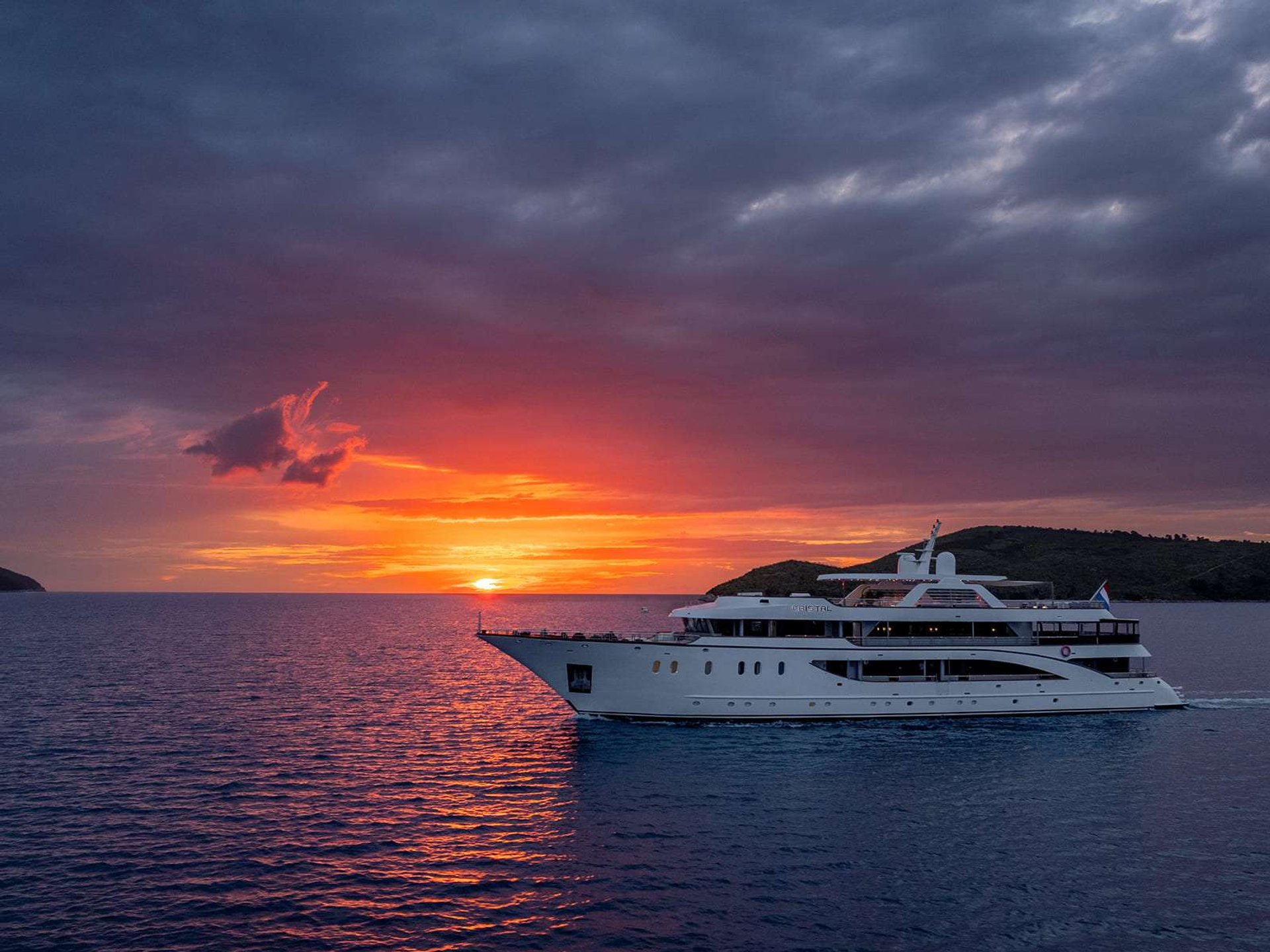 A crewed motor yacht silhouetted against a dramatic Adriatic sunset.