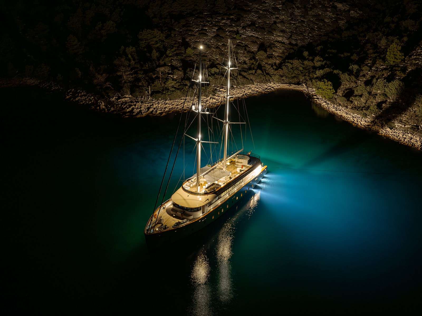 A crewed yacht lit up at night in a quiet Dalmatian harbor.