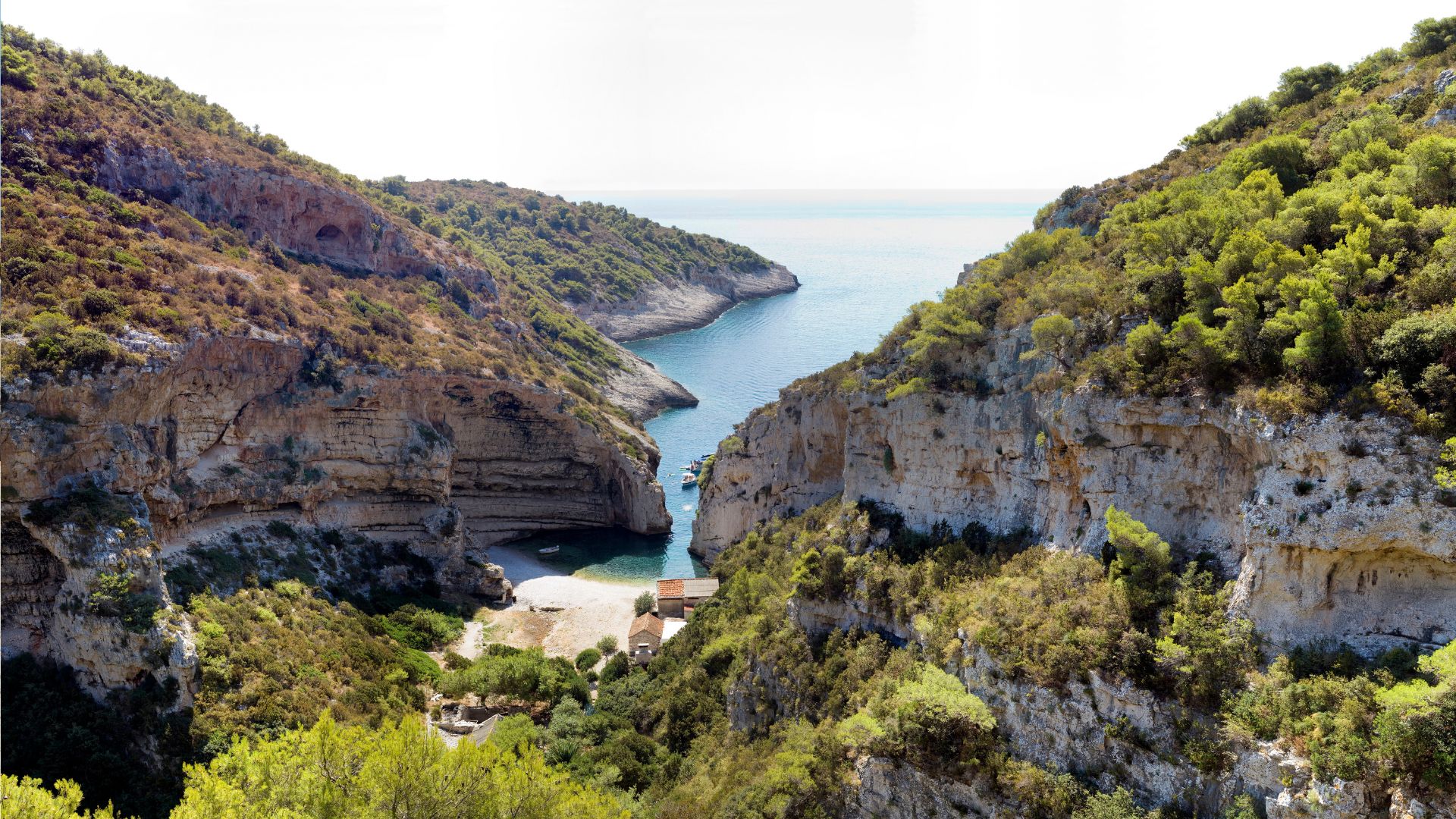 Stiniva Bay on Vis, a narrow cleft between two limestone cliffs opening onto a pebble beach.