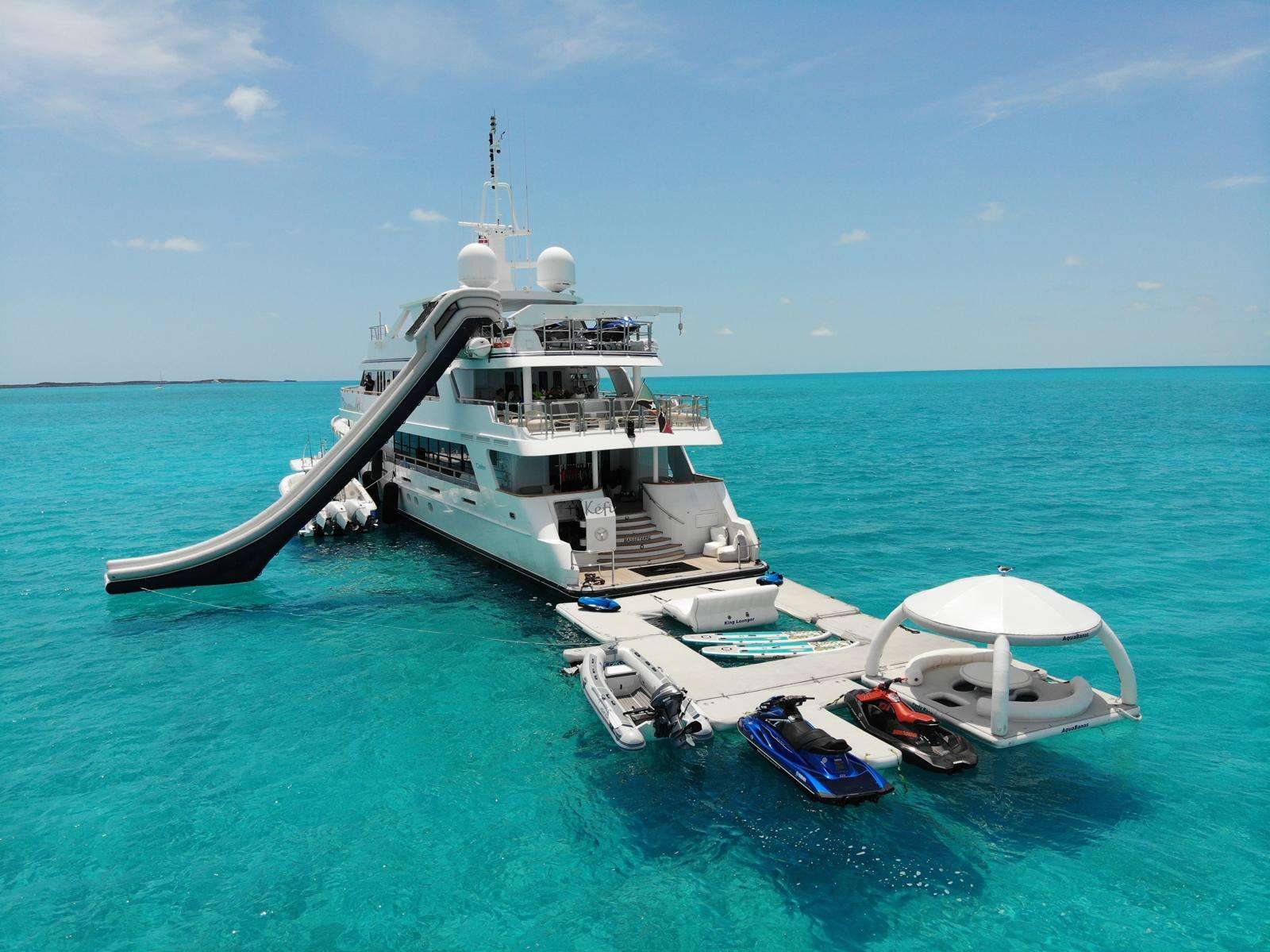 The yacht holds in deeper water nearby, slide and toys deployed.