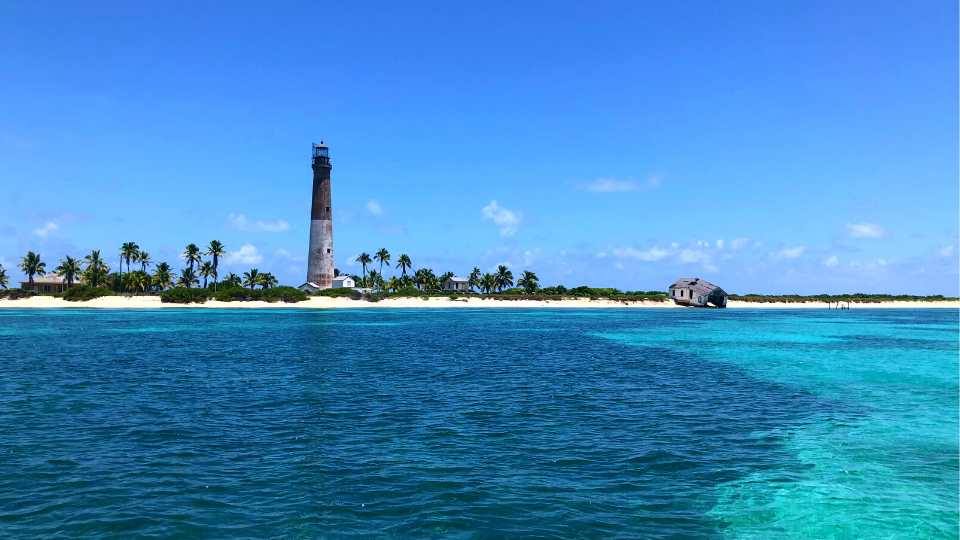 Loggerhead Key's lighthouse over palms and white sand, a grounded wreck structure on the beach beyond