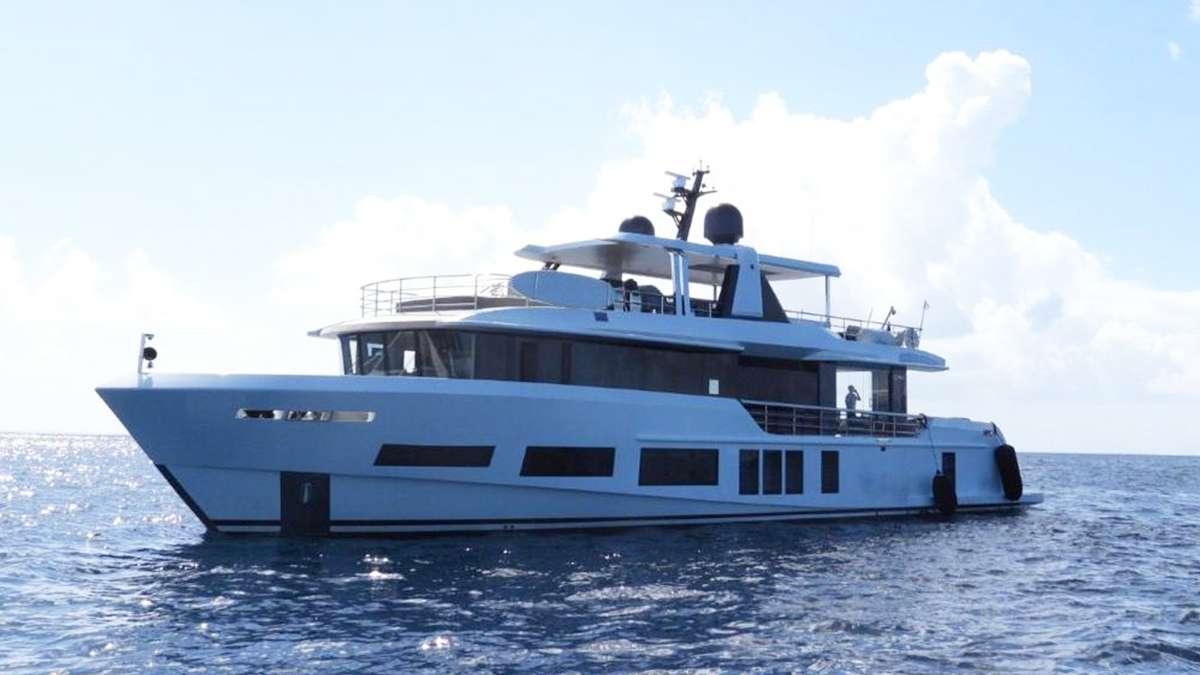 Crewed motor yacht lying in open water, flybridge shaded and tender davits aft
