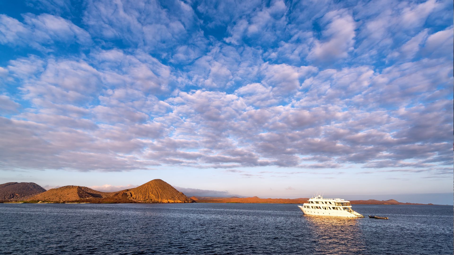 Expedition yacht at anchor at golden hour, volcanic hills behind