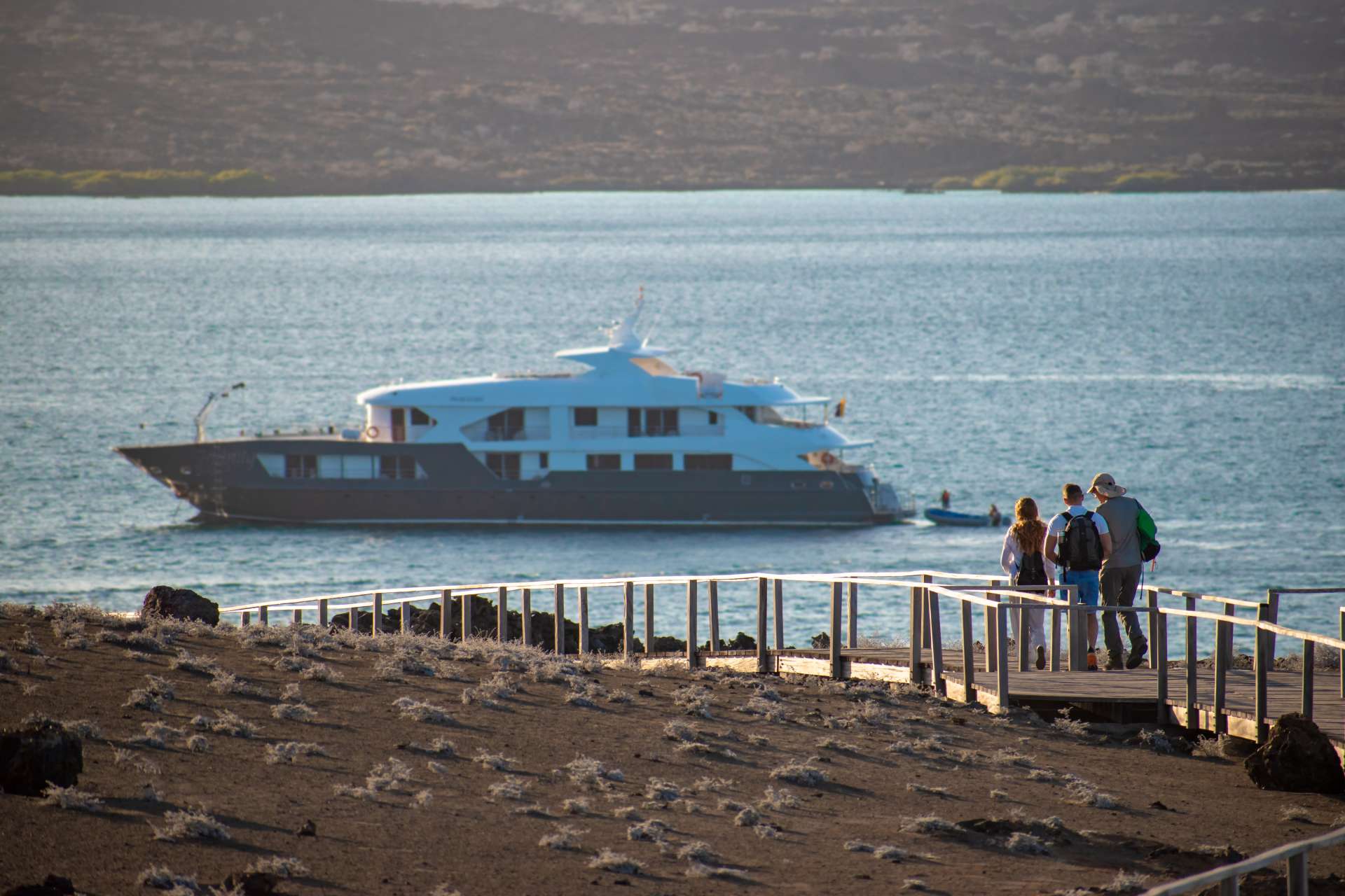 Yacht offshore, guests walking the lava boardwalk — the Egas Port pattern.