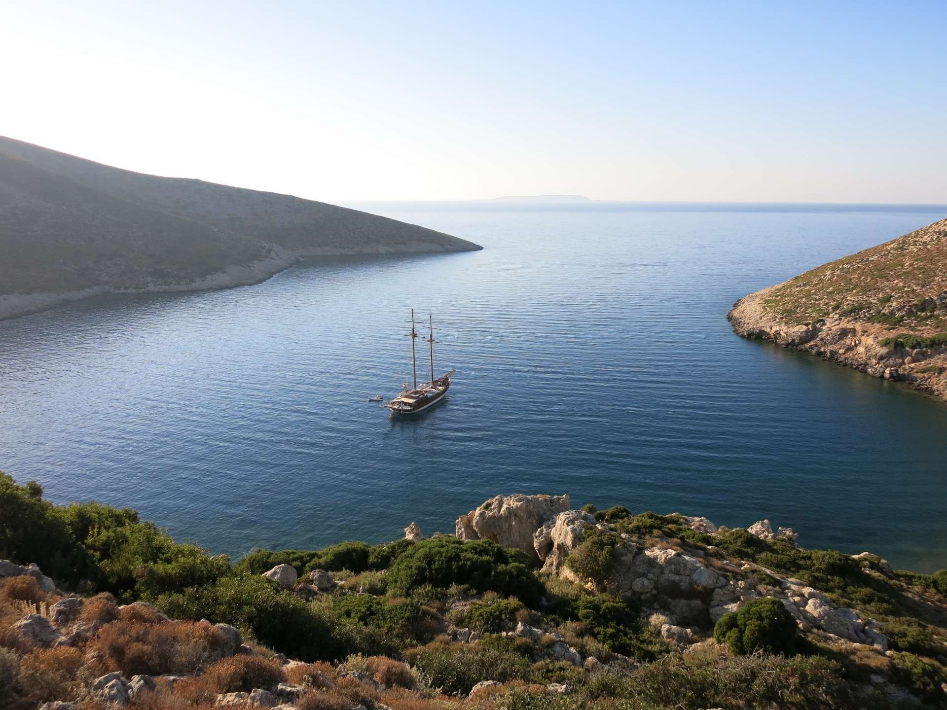 A typical Cycladic anchorage—a quiet bay cut into barren hills, a yacht on the hook, the Meltemi blocked by the island itself.
