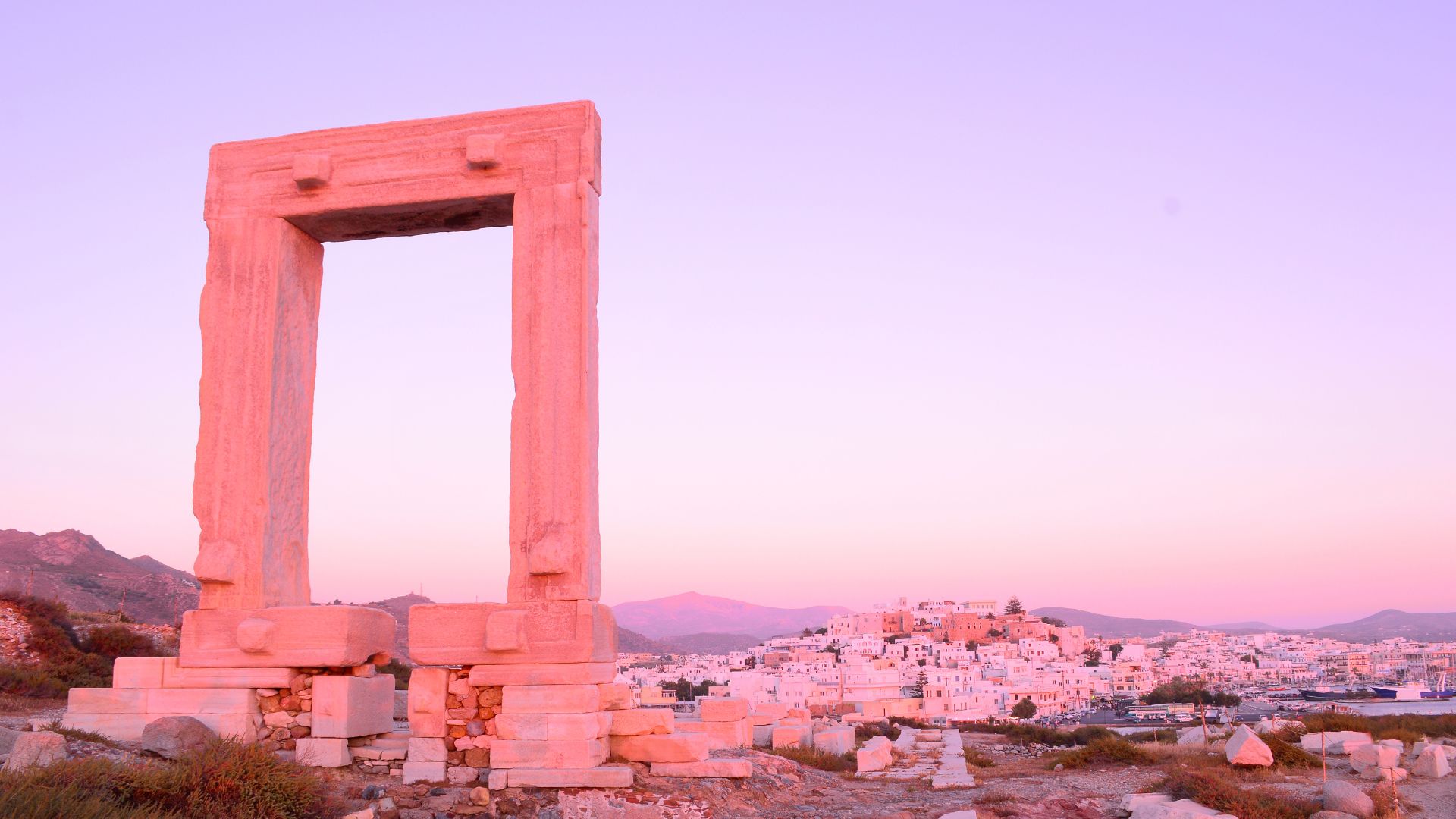 The Portara marble temple gate on Naxos, silhouetted against a pink sunset sky.