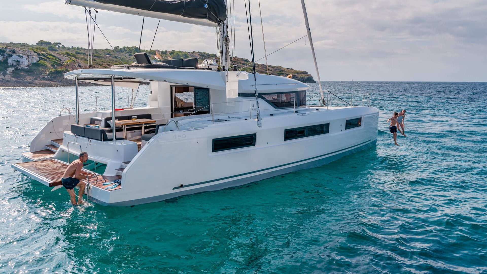Modern crewed catamaran at anchor — guests jumping off the swim platform into clear Adriatic water