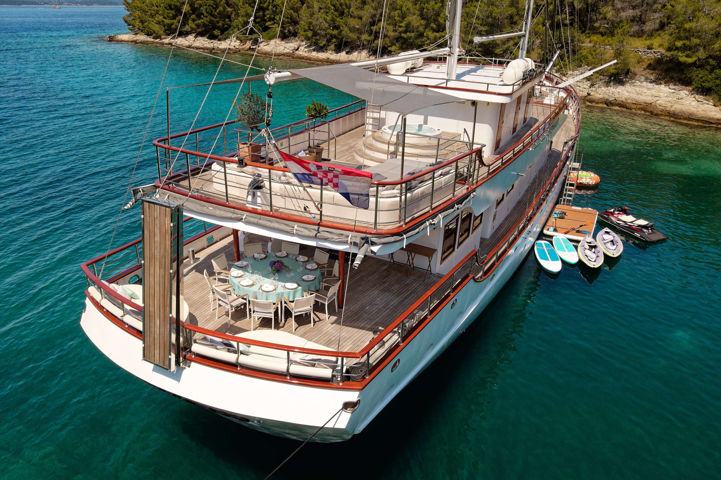 Aft-deck dining table set on a wooden crewed gulet — flowers, white linen, the Adriatic over the stern