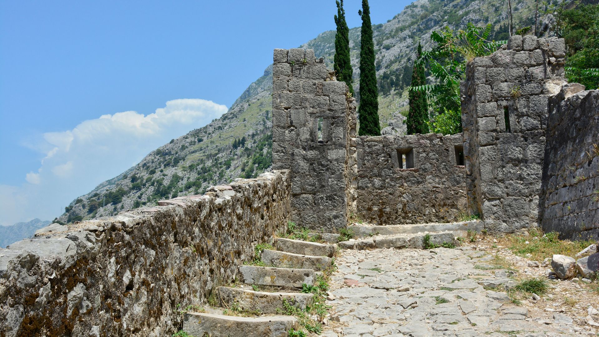 Up on Kotor's medieval wall climb — stone steps and a ruined chapel above the Old City, with the limestone face of Mt. Lovćen rising behind