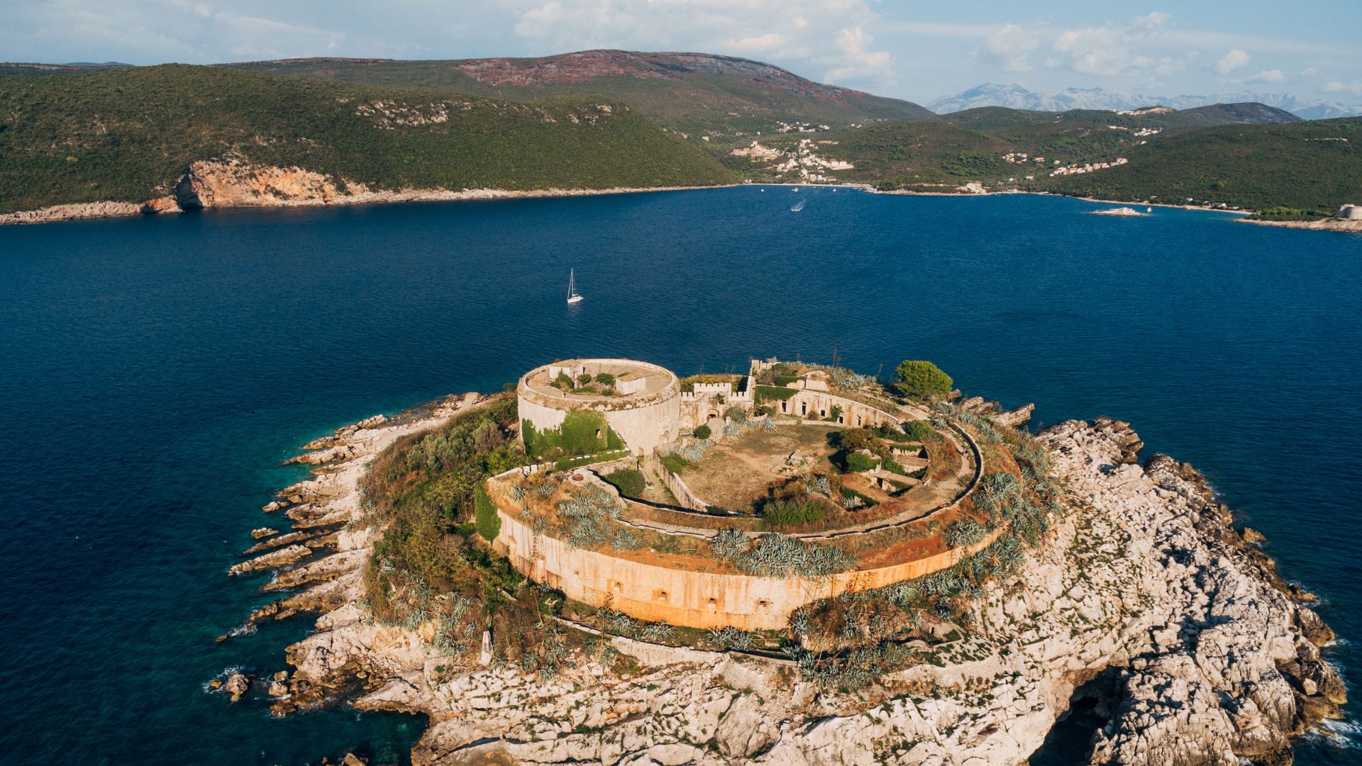 Mamula Island — the circular 19th-century Austro-Hungarian sea-fortress at the bay's mouth, used as a Yugoslav internment camp during WWII, reopened in 2023 as a Marriott Autograph Collection hotel. The wellness focus is current; the history is acknowledged.
