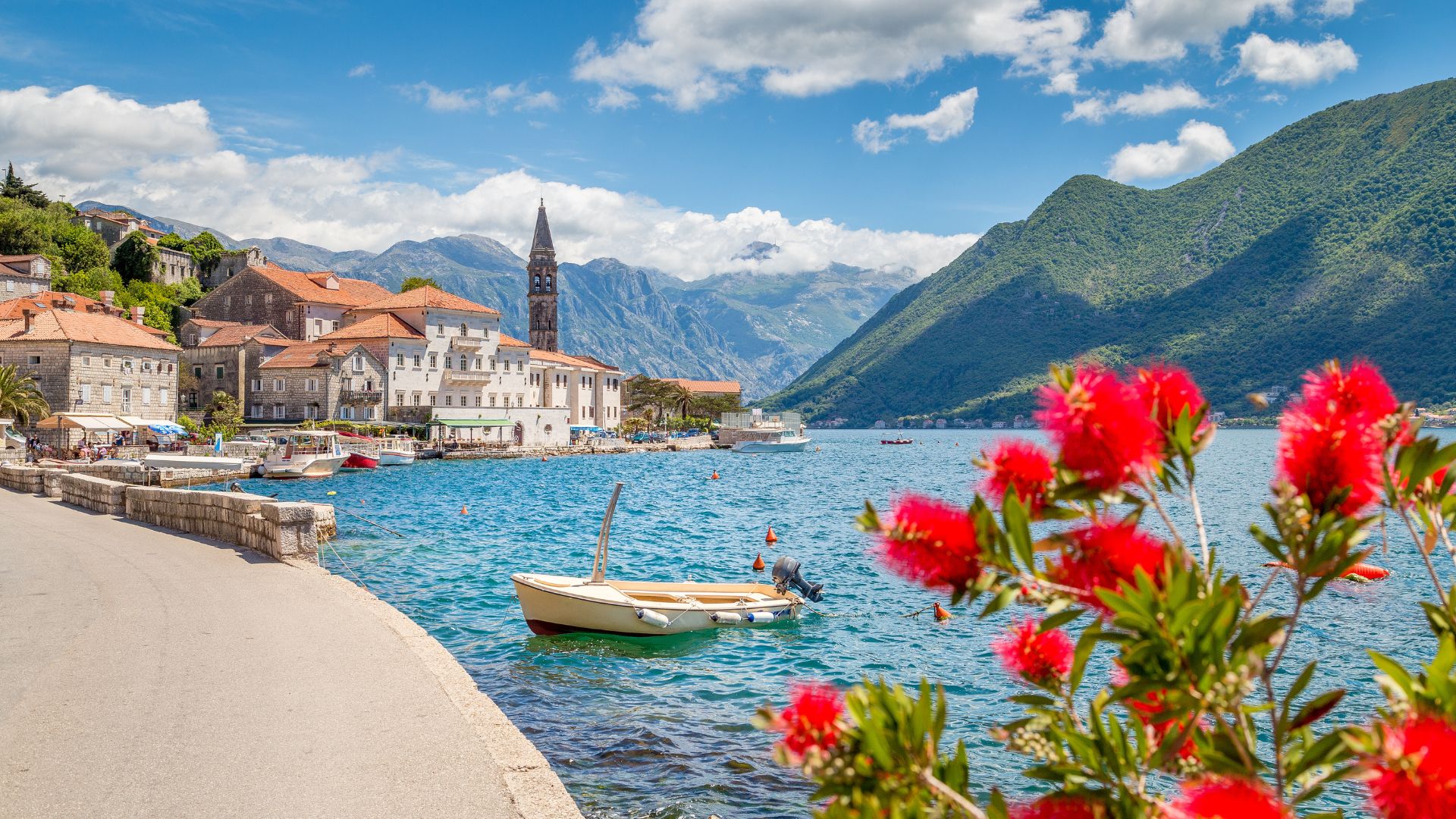 Perast's waterfront promenade — twenty minutes end to end. The bell tower of St. Nicholas marks the town's center; restaurants and the maritime museum line the water.