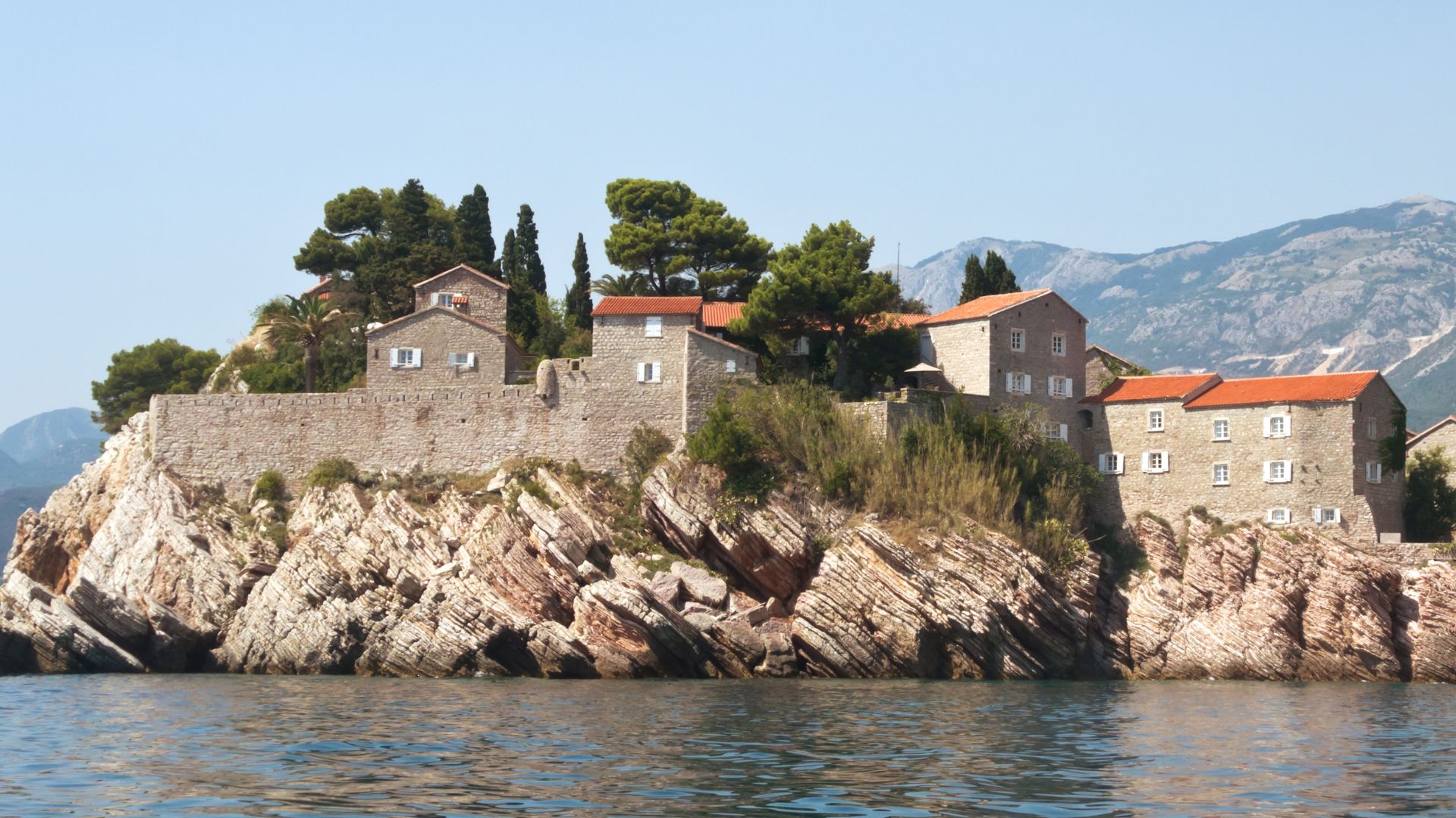 Sveti Stefan from sea level — fortified medieval island walls and pines on the rocky base