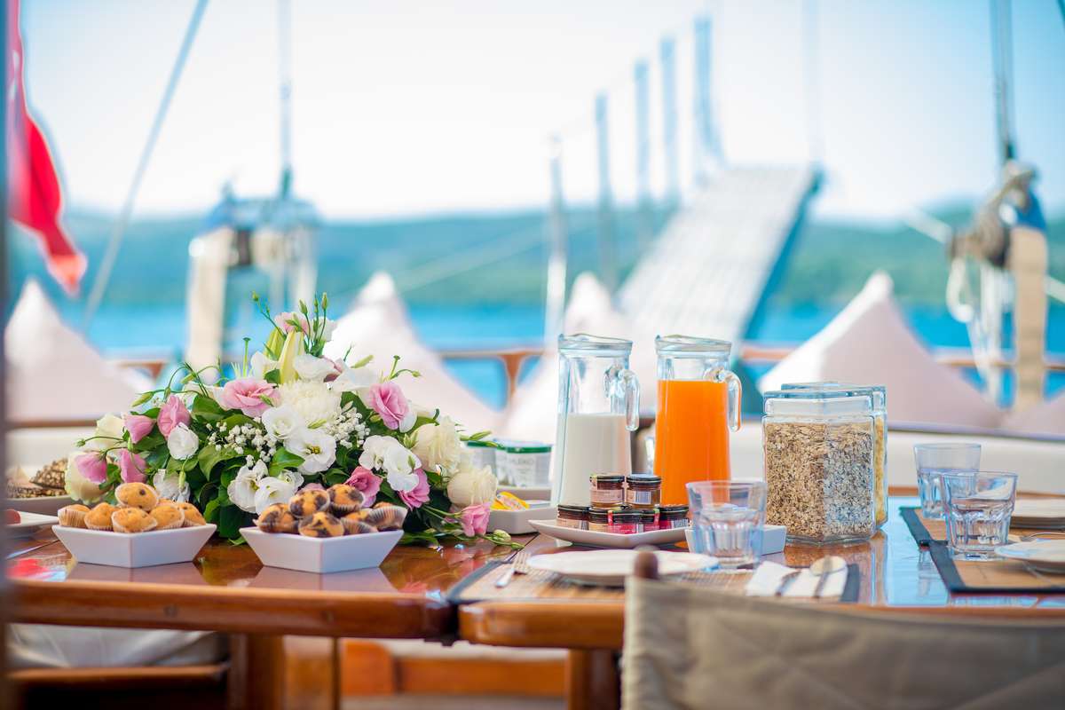 Aft-deck breakfast aboard a wooden gulet — fresh pastries, juice, flowers, the morning Adriatic light astern