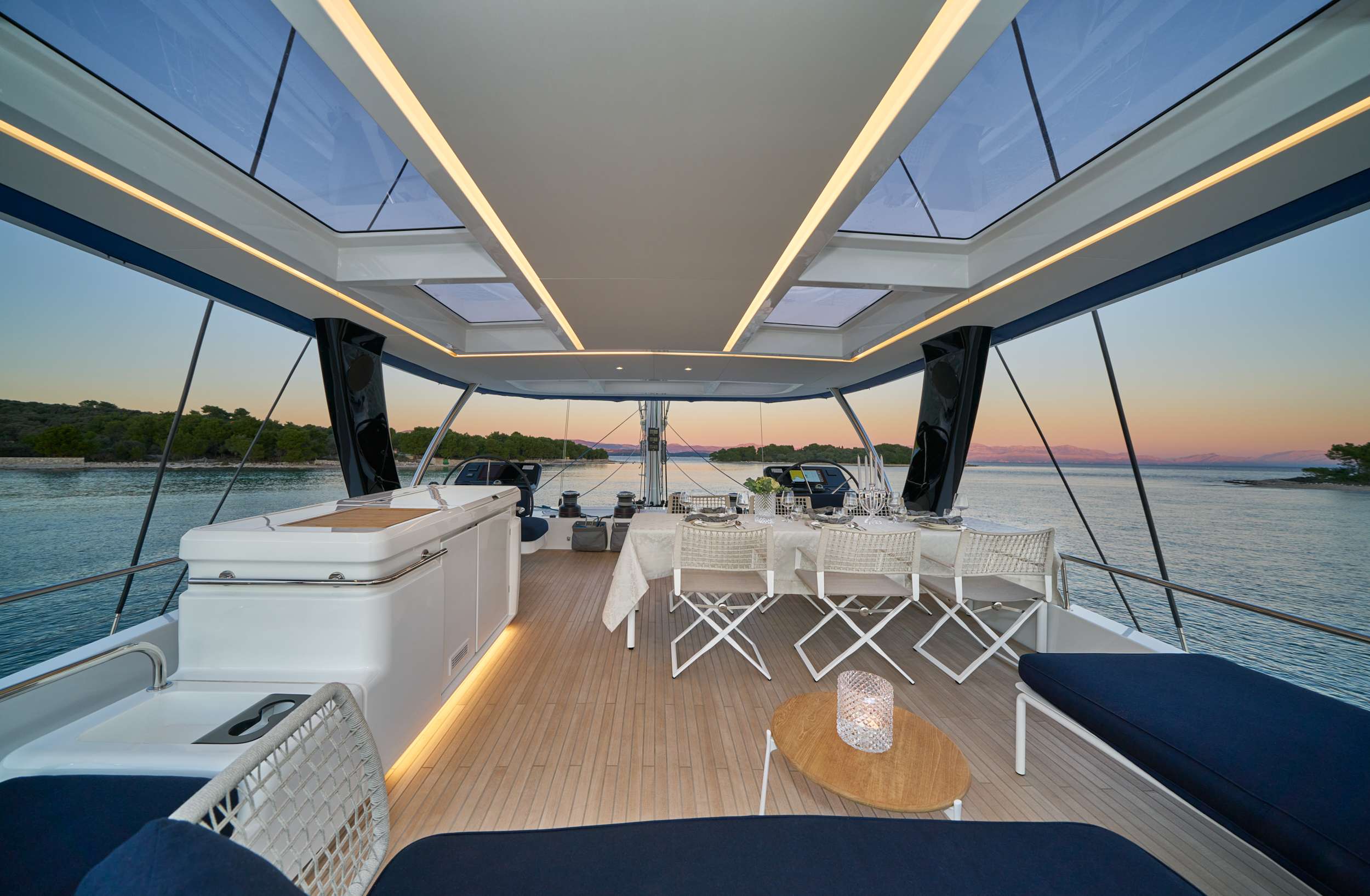 Aft-deck of a modern crewed yacht at dusk — glass roof panels, the Mediterranean horizon turning pink