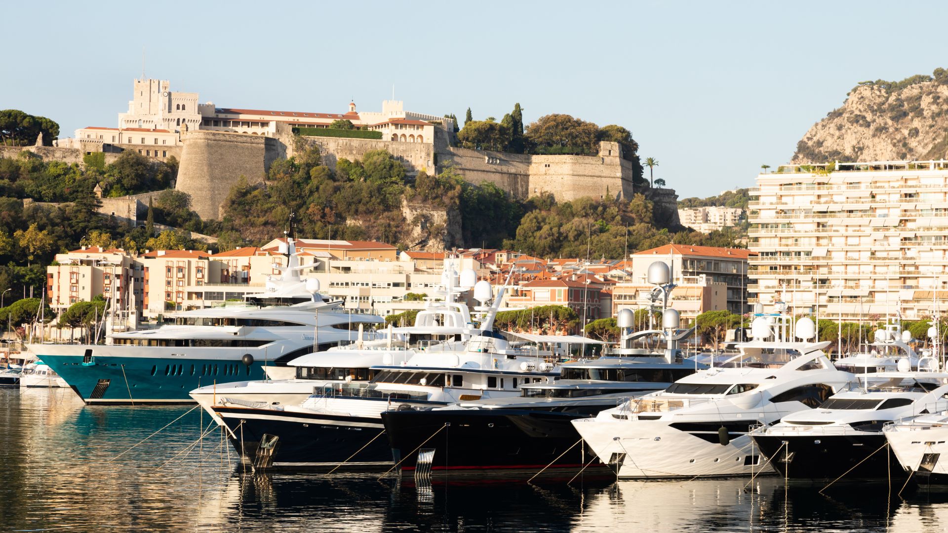 Monaco's Port Hercule from the harbor — megayachts on the quay with Monte-Carlo above.