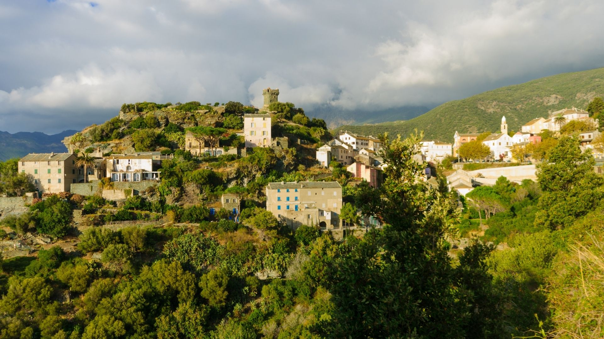Nonza's beach is black volcanic rock — leftover from a former asbestos quarry that closed in the 1960s. The village above it sits on a clifftop with a single Genoese tower and a vertical-ladder access to the beach.
