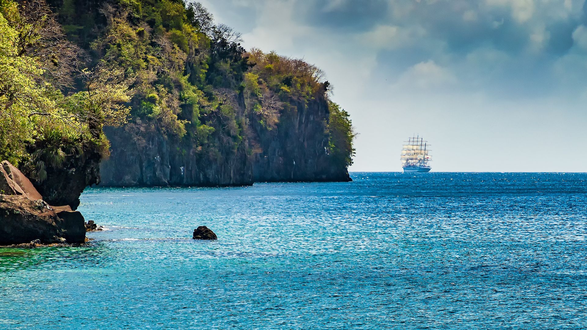 Running down St. Vincent's leeward coast — steep green cliffs falling straight to the sea, a tall ship standing off the headland. The boat keeps moving; the island is the scenery.